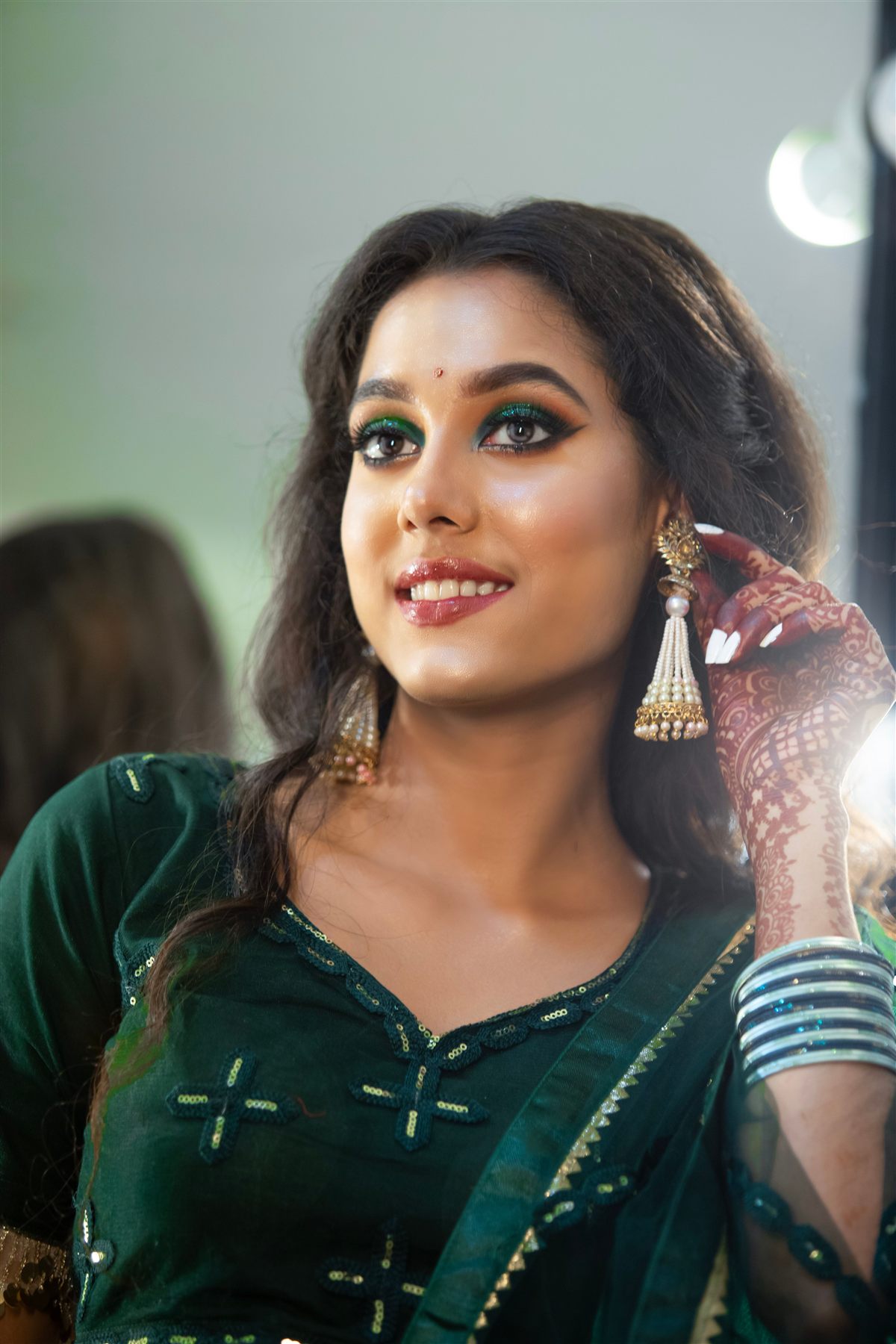 Bride in an emerald green saree with fresh mehndi and jhumka earrings, makeup by Bellamira Beauty Studio
