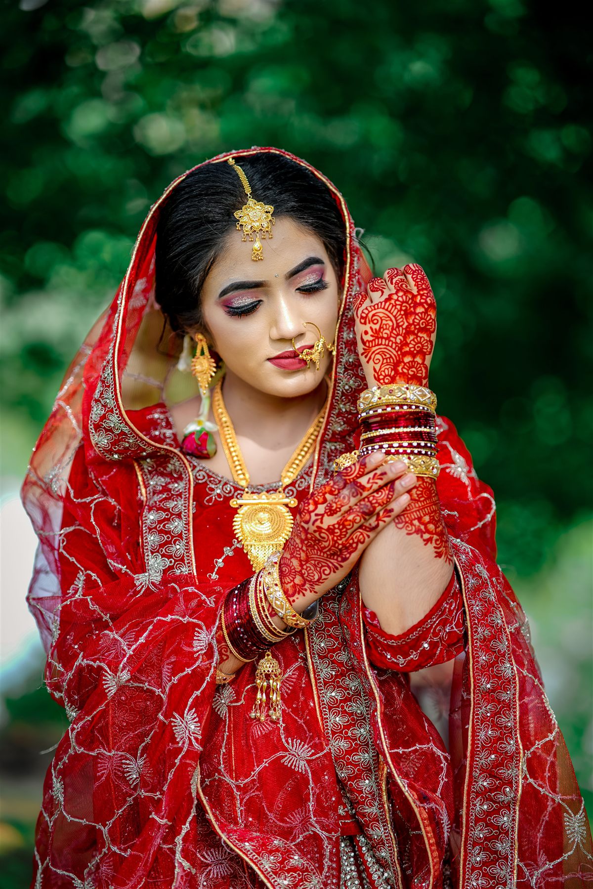 Bride in a red and gold lehenga with maang tikka, nath and bridal henna, makeup by Bellamira Beauty Studio