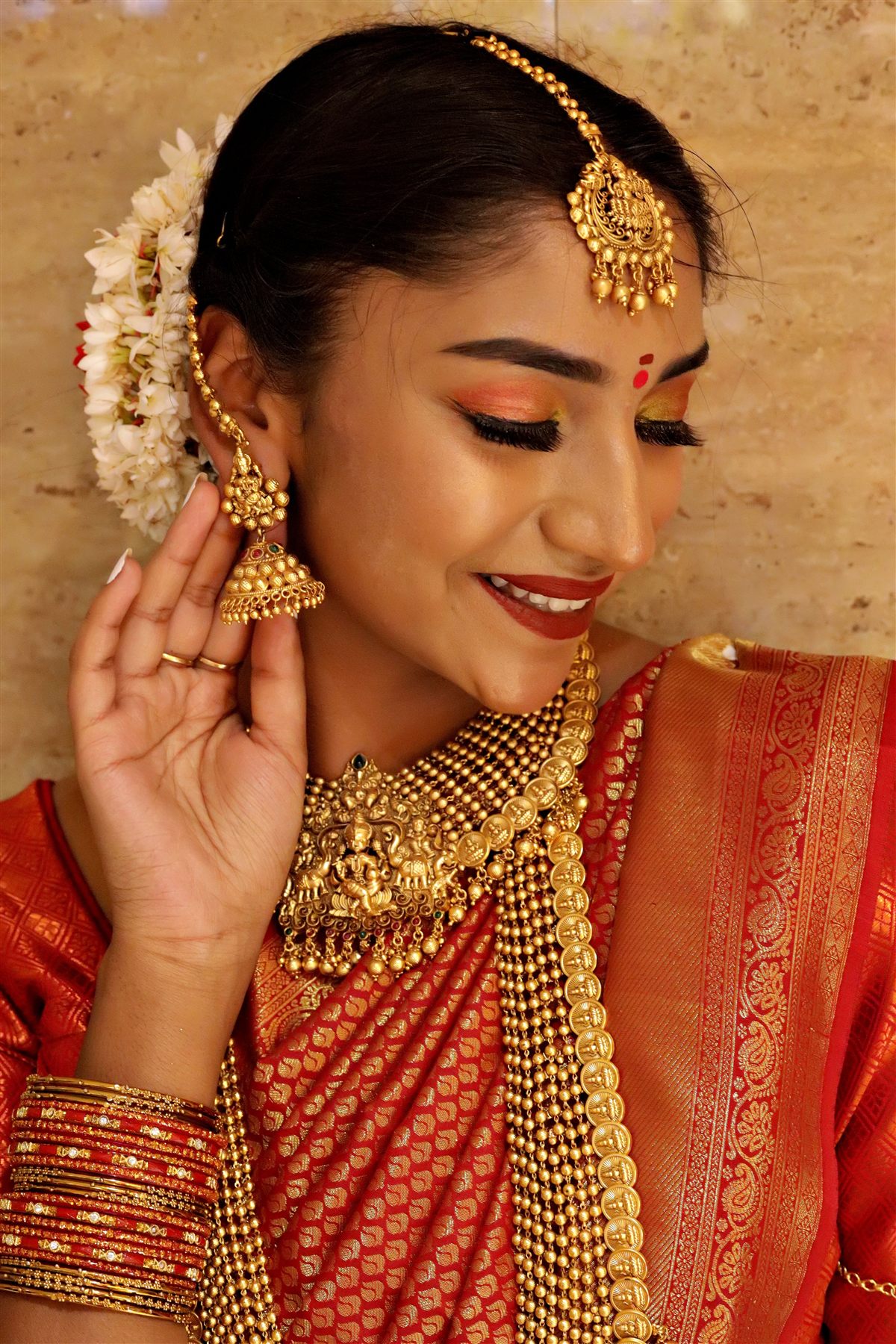 South Indian bride in a red and gold silk saree with temple jewellery and jasmine in her hair, bridal makeup by Bellamira Beauty Studio